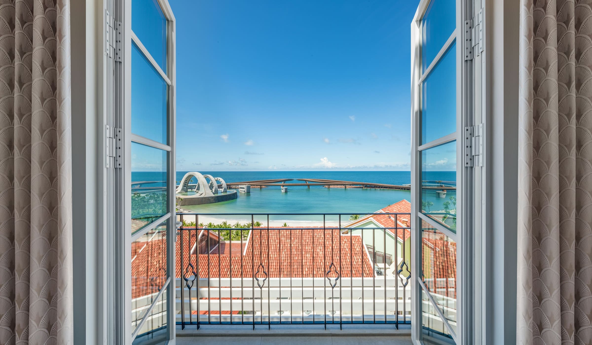 Open balcony doors with a view of the sea and terracotta roofs